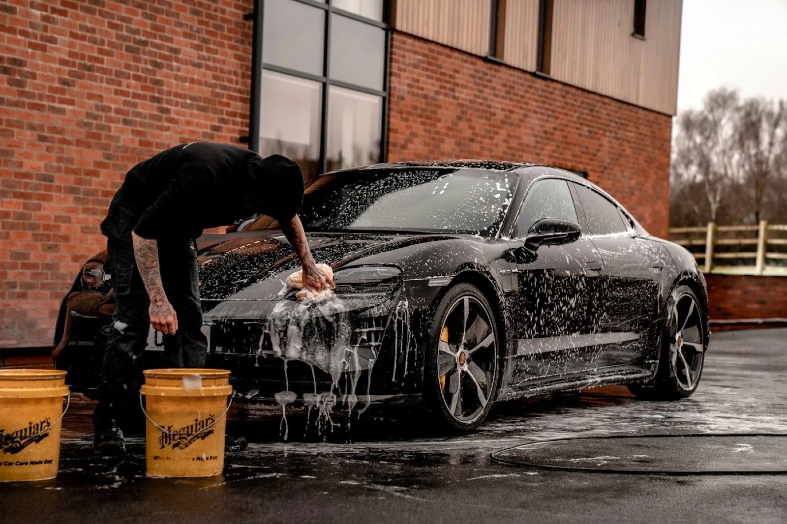 Detailer hand-washing a dark car with foam